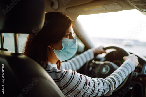 Young woman driving car with protective mask on her face. The concept of preventing the spread of the epidemic and treating coronavirus, pandemic in quarantine city. Covid -19. © maxbelchenko