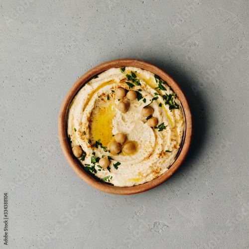 Large bowl of homemade hummus garnished with chickpeas, red sweet pepper, parsley and olive oil