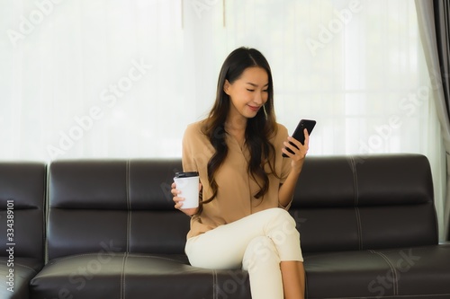 Portrait beautiful young asian woman use mobile smartphone or cellphone with coffee cup on sofa living room