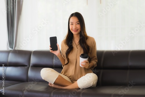 Portrait beautiful young asian woman use mobile smartphone or cellphone with coffee cup on sofa living room