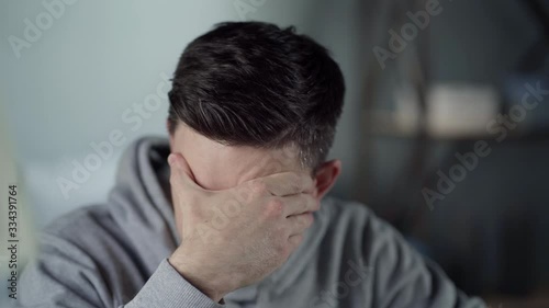 Work from home. Tired young white man is concentrating on the laptop and touches his forehead