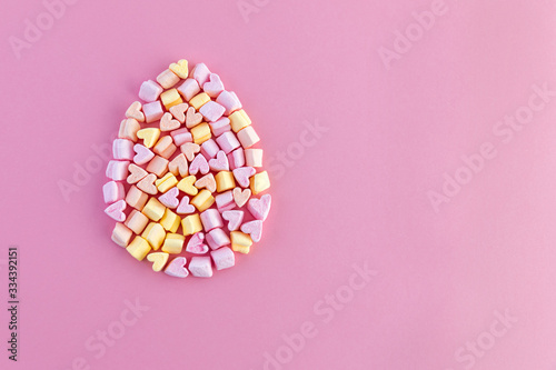 Easter egg shape from multi-colored little marshmallows hearts on a pink background. Concept. Copy space