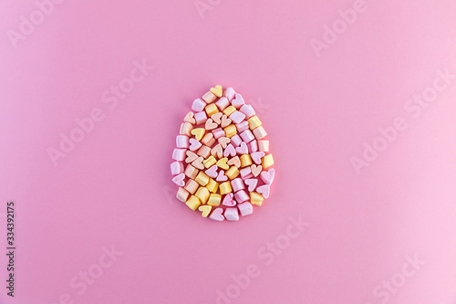 Single multicolored easter egg made of small marshmallows hearts on a pink background. Concept.