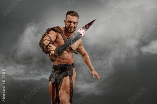 Wounded gladiator attacking with sword covered in blood on background drammatic sky photo