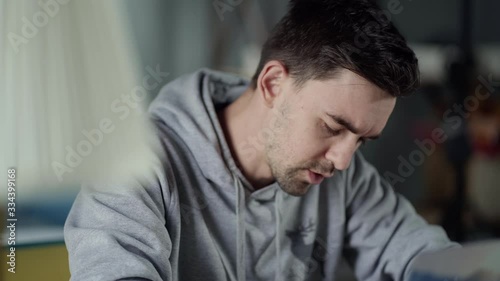 Moving shot at tired young white man is concentrating on the laptop сoughs and touches his forehead. Work from Home. 