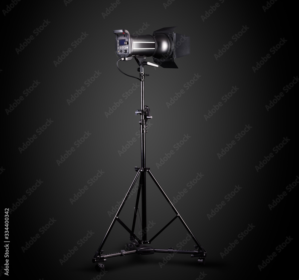 Photography studio flash on a lighting stand isolated on black background.