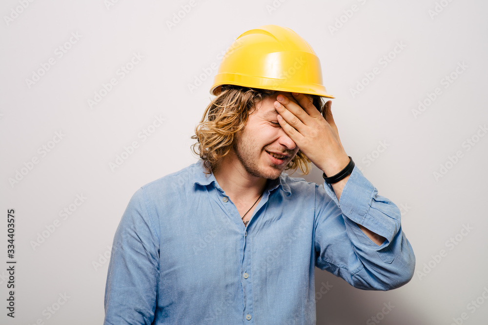 Tired young manual worker - builder, isolated on gray background, close-up studio shot Tired young manual worker - builder, isolated on gray background, close-up studio shot