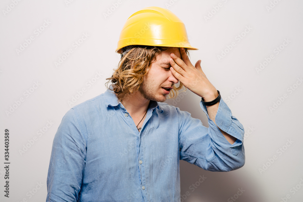 Tired young manual worker - builder, isolated on gray background, close-up studio shot Tired young manual worker - builder, isolated on gray background, close-up studio shot