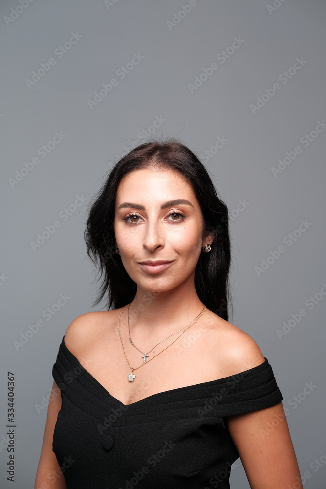 A large portrait of a middle-aged woman (30-35 years old) with dark hair and brown eyes in a black dress on a light background. A large portrait of a middle-aged woman (30-35 years old) with dark hair and brown eyes in a black dress on a light background.