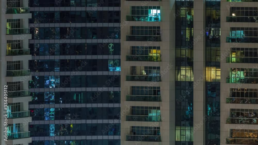Rows of glowing windows with people in the interior of apartment building at night. Modern skyscraper with glass surface. Concept for business and modern life. Pan right Rows of glowing windows with people in the interior of apartment building at night. Modern skyscraper with glass surface. Concept for business and modern life. Pan right