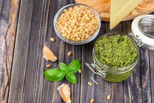 Pesto sauce in a jar with pine nuts, parmesan and garlic over dark wooden background