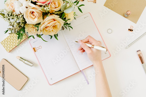 Hand wtite in pink opened notebook on white background. Tender mood and blogging concept with beautiful roses bouquet and accesoires in flat lay style photo