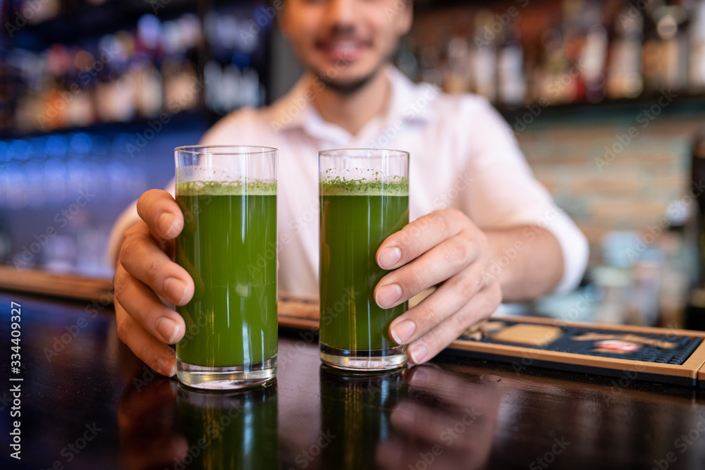 Hands of young waiter or barman holding two glasses of green vegetable cocktail