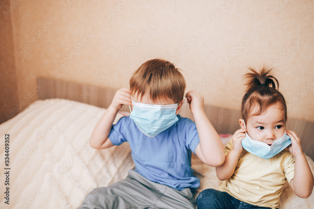 Two children brother and sister in medical masks using laptop, home education, stay at home.