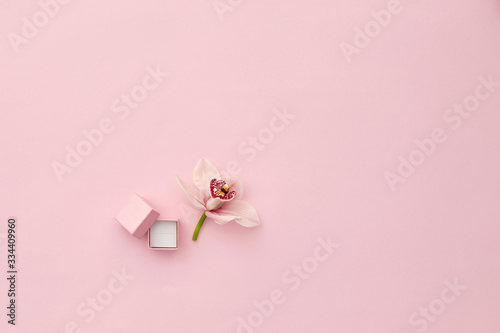 Pink box for an engagement ring and orchid flower on pink background, top view. Space for text © producer