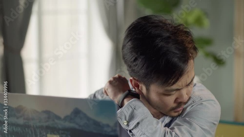 Work from home. Sick and tired young Korean man with a mustache and a beard sits at a desk, working on a laptop at home and coughs