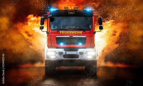 Feuerwehrfahrzeug mit Blaulicht und mit Flammen im Hintergrund