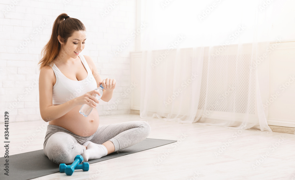 Young pregnant woman drinking water during yoga training Young pregnant woman drinking water during yoga training