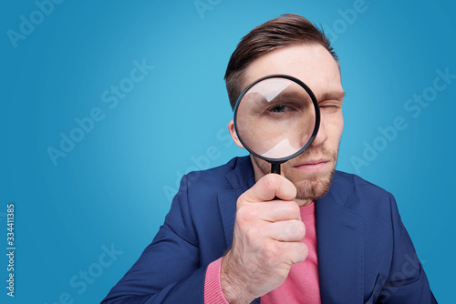 Serious young male detective holding magnifying glass by right eye