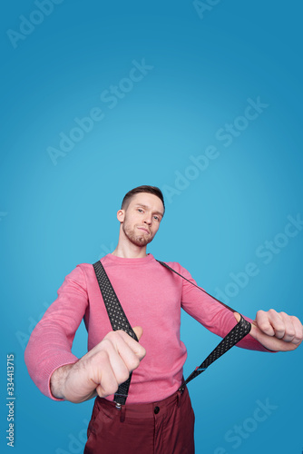 Young handsome man in pink casual pullover and pants stretching suspenders