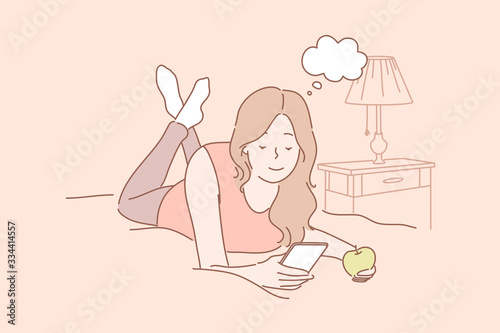 Online communication, social media or network concept. Young woman or girl laying on bed at home eating apple and chatting online using smartphone. Watching videos. Social media, network communication