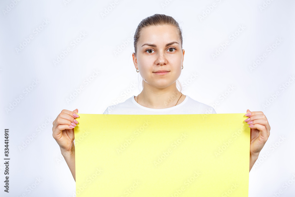 A girl in a white T-shirt is holding a yellow blank large sheet of banner. A girl in a white T-shirt is holding a yellow blank large sheet of banner.
