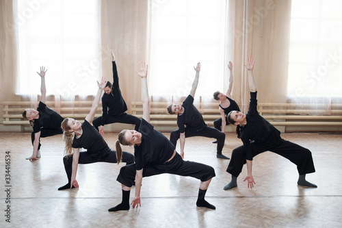 Large group of young fit people in black activewear exercising together