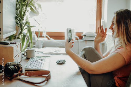 Happy young woman waving hands to greeting partner during making video conference with her team. 