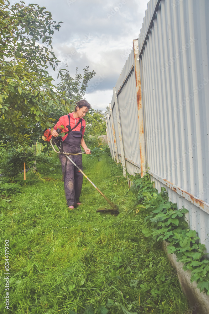 female worker mows the grass with a trimmer in the garden female worker mows the grass with a trimmer in the garden