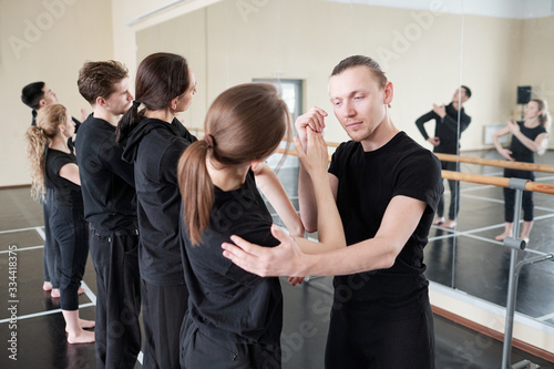 Young instructor of modern ballet dancing cource helping one of his students