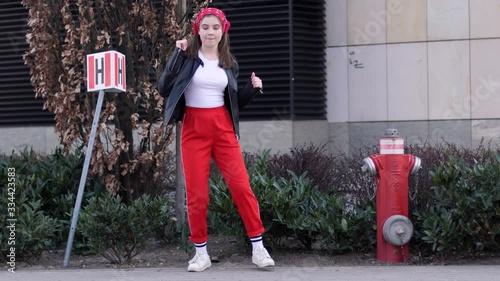 Good mood teenager cute girl walk and dance on city street wearing red pants