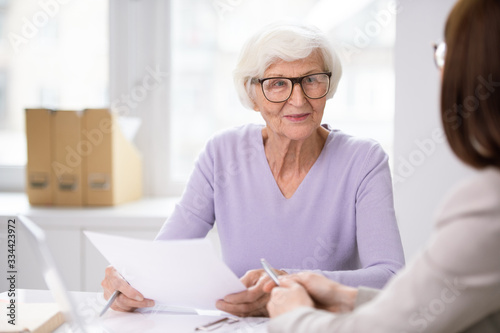 Senior smiling female client with insurance form listening to her agent