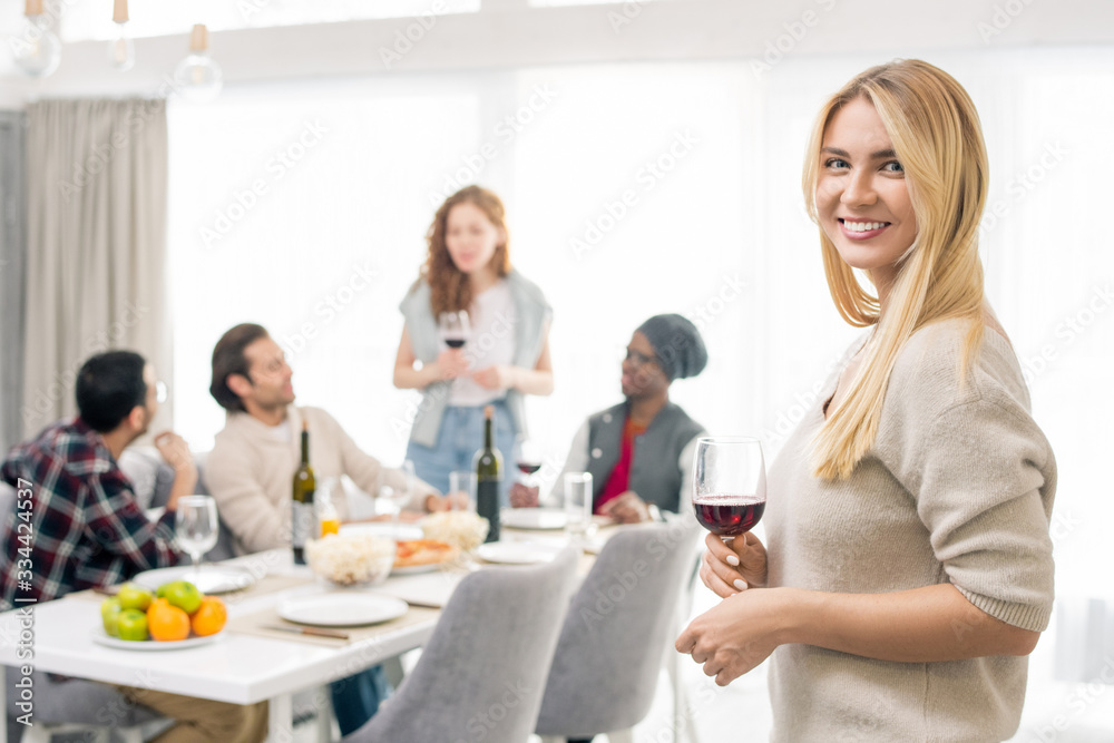 Young smiling woman with glass of wine on background of intercultural friends