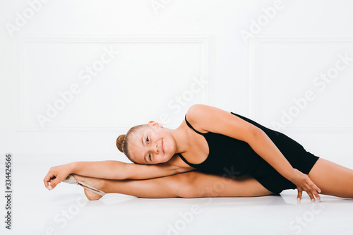 Young girl in a black dress in gymnastic pose doing splits lying on one leg