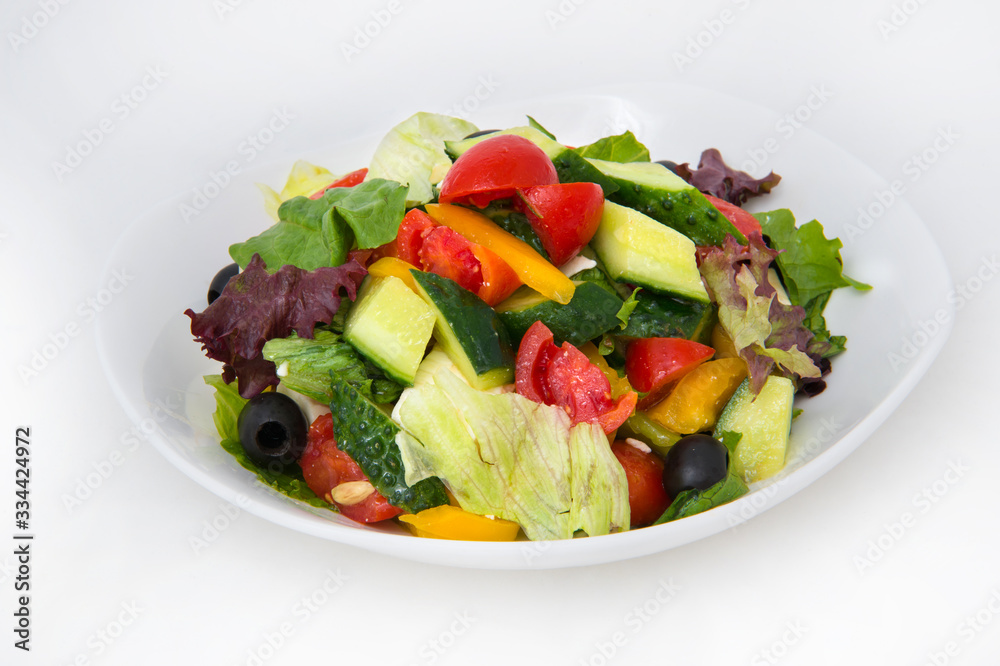 Salad of red and yellow tomatoes, cucumbers, cabbage, greens and olives with vegetable oil in a deep white plate on a white background