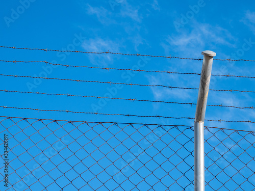 Barbed wire from a security fence attached to a metal frame with a blue sky in the background
