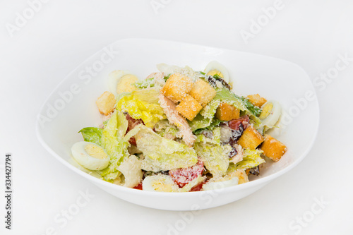 Salad in a deep white plate of cabbage, tomato, crackers, pieces of chicken breast, eggs, grated cheese