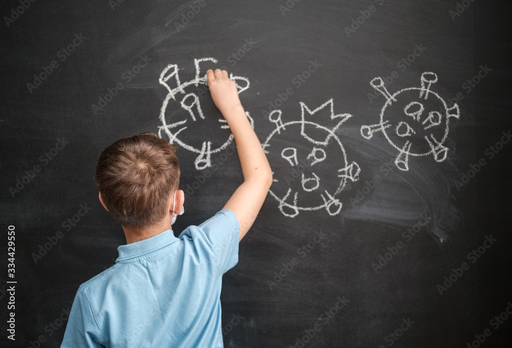 a boy in a medical mask draws a coronavirus on a blackboard with chalk. the concept of the covid-19 pandemic and online training during quarantine