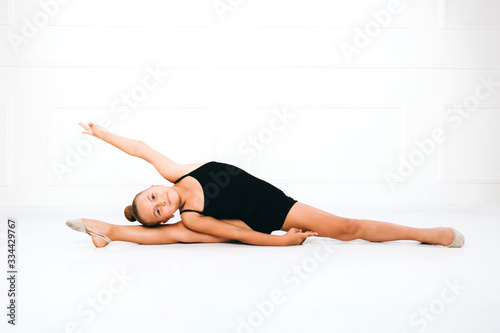 Young girl in a black dress in gymnastic pose doing splits, lying on one leg, holding arm up