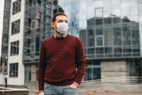 portrait of brunette man in a surgical bandage on a background of a modern building, coronavirus, illness, infection, quarantine, medical mask