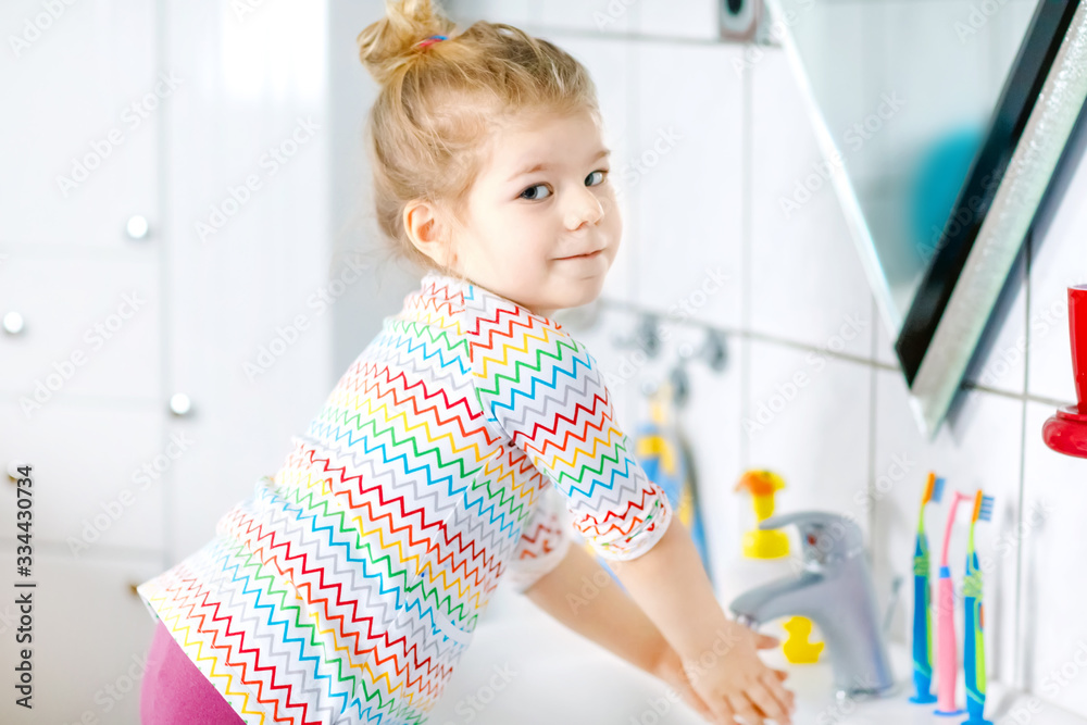 Cute little toddler girl washing hands with soap and water in bathroom. Adorable child learning cleaning body parts. Hygiene routine action during viral desease. kid at home or nursery. Cute little toddler girl washing hands with soap and water in bathroom. Adorable child learning cleaning body parts. Hygiene routine action during viral desease. kid at home or nursery.