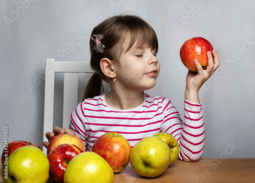 Apples lie on the table, little girl sniffs an apple