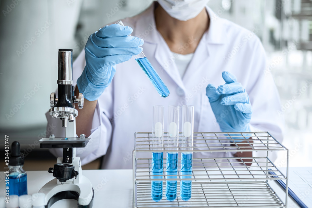 Fototapeta premium Biochemistry laboratory research, Scientist or medical in lab coat holding test tube with Using Microscope reagent with drop of color liquid over glass equipment working at the laboratory