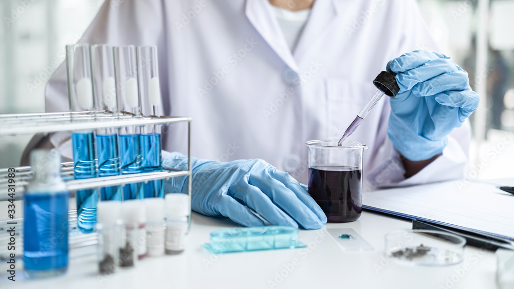 Scientist or medical in lab coat holding dropper with reagent, mixing reagents in glass flask, glassware containing chemical liquid, laboratory research and testing of Microscope