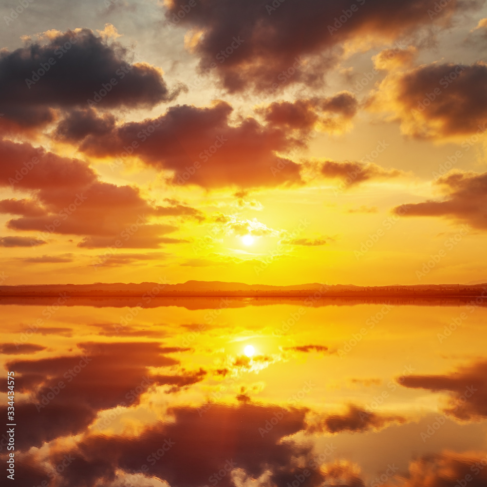 Beautiful sunset landscape with a lake, dramatic golden sky above reflects in the water.