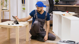 Male worker in overalls assembles new white furniture