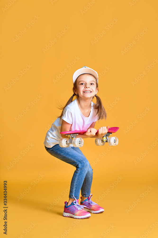 Stylish funny girl wearing white t-shirt, blue jeans and sneakers, holding skateboard over yellow background. Stylish funny girl wearing white t-shirt, blue jeans and sneakers, holding skateboard over yellow background.