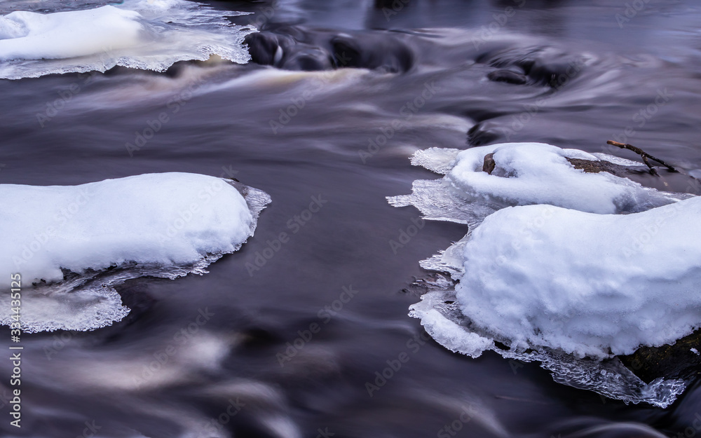Winter landscape. River flows through ice and snow.