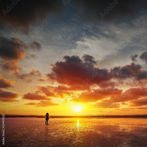 Person takes a photo of beautiful sunset landscape with a lake, dramatic golden sky above reflects in the water.