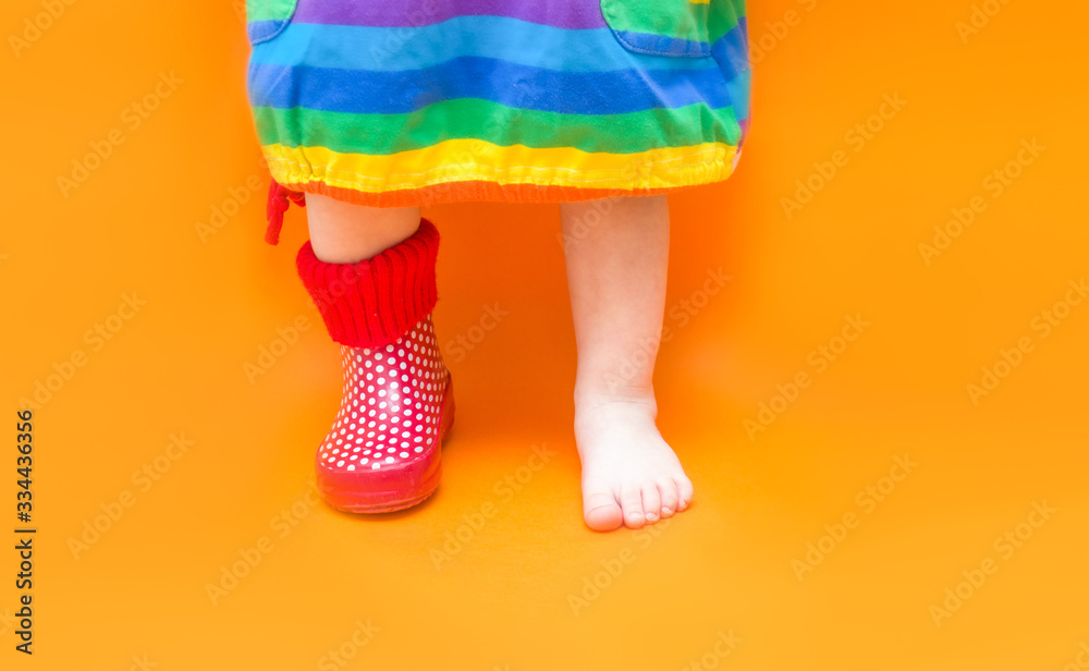 Children's foot in one rubber boot. One leg is bare barefoot. Baby